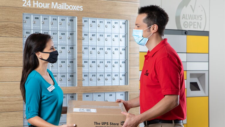 Customer at a UPS Store getting handed their package from an employee. 