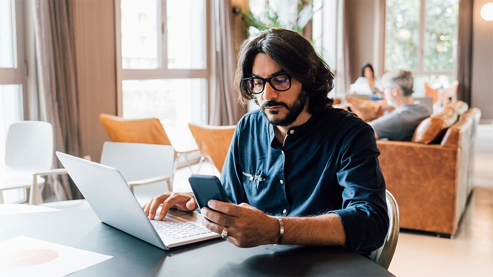 Hombre revisando una computadora portátil y un dispositivo móvil.