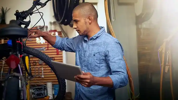 A man taking notes on his iPad as he inspects his bicycle