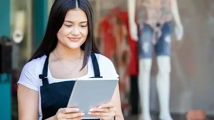 Young woman standing outside of clothing store looking at a tablet